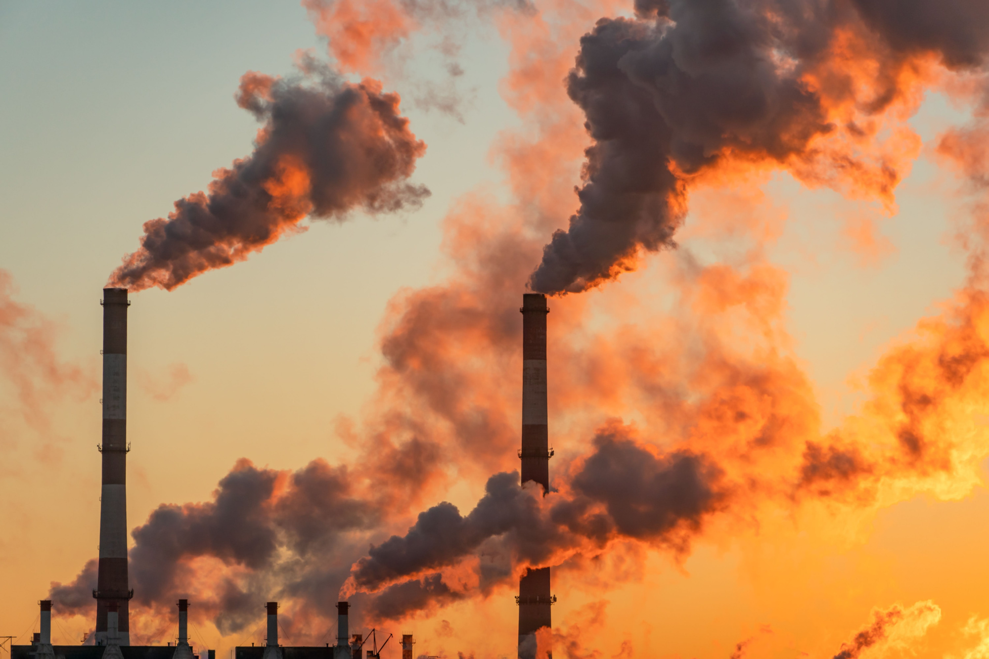 smoke stacks emitting pollutants in front of a sunrise