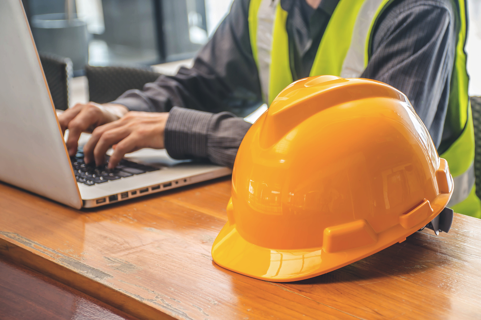 worker in safety vest working on laptop with hard hat on desk